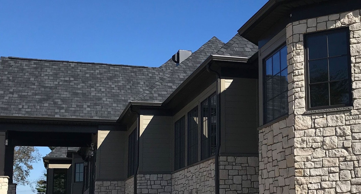 Beautiful home with professionally installed seamless gutters featuring dark siding and stone accents